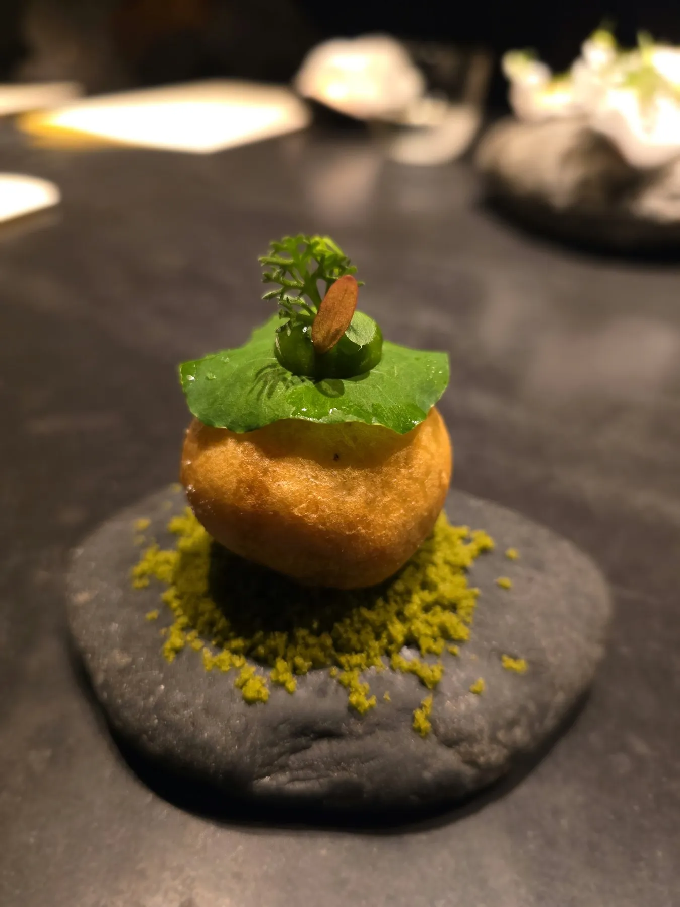 Fried sphere with a green herb top on a black stone, close up