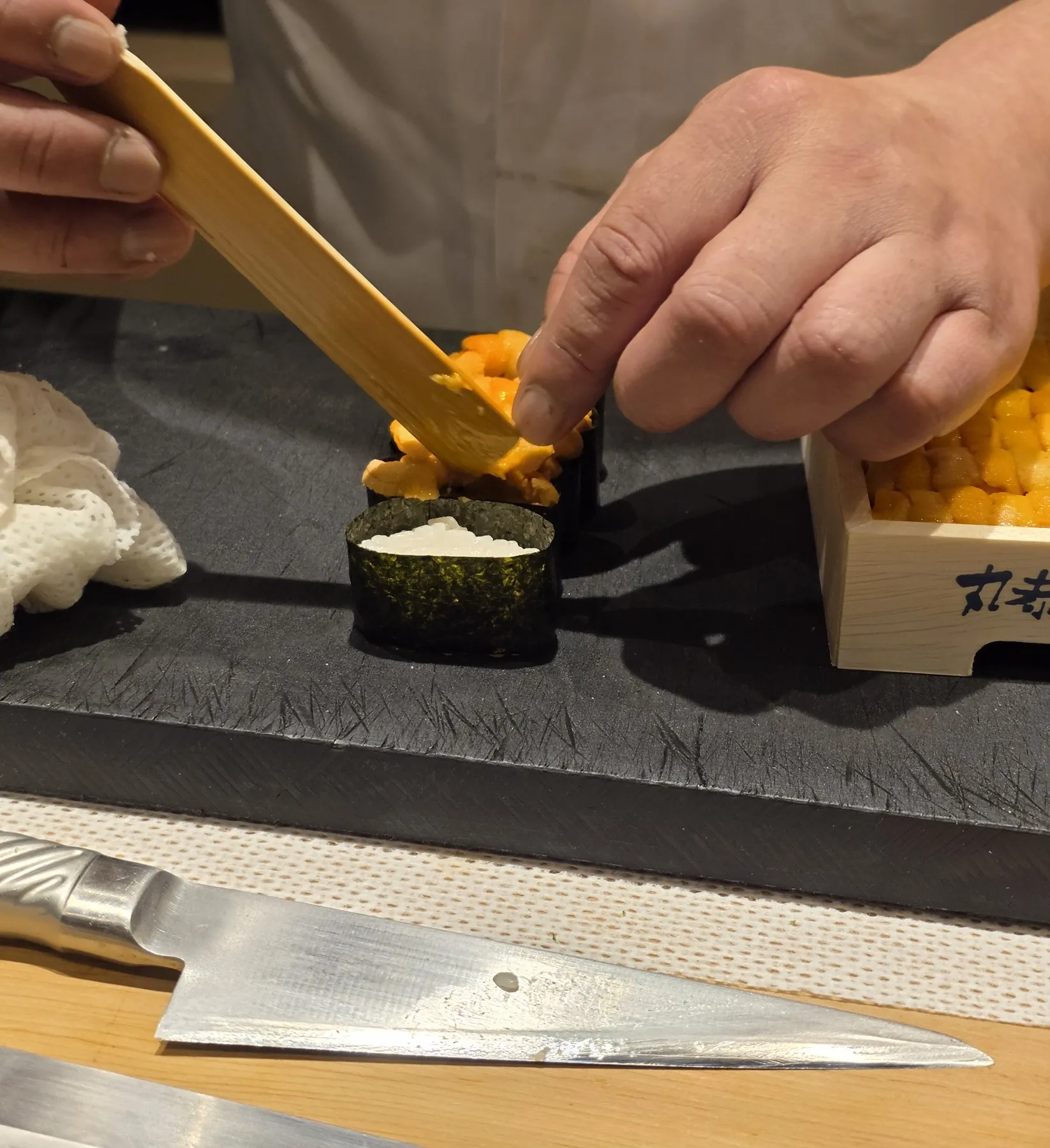 Chef's hands packing uni into a nori cup