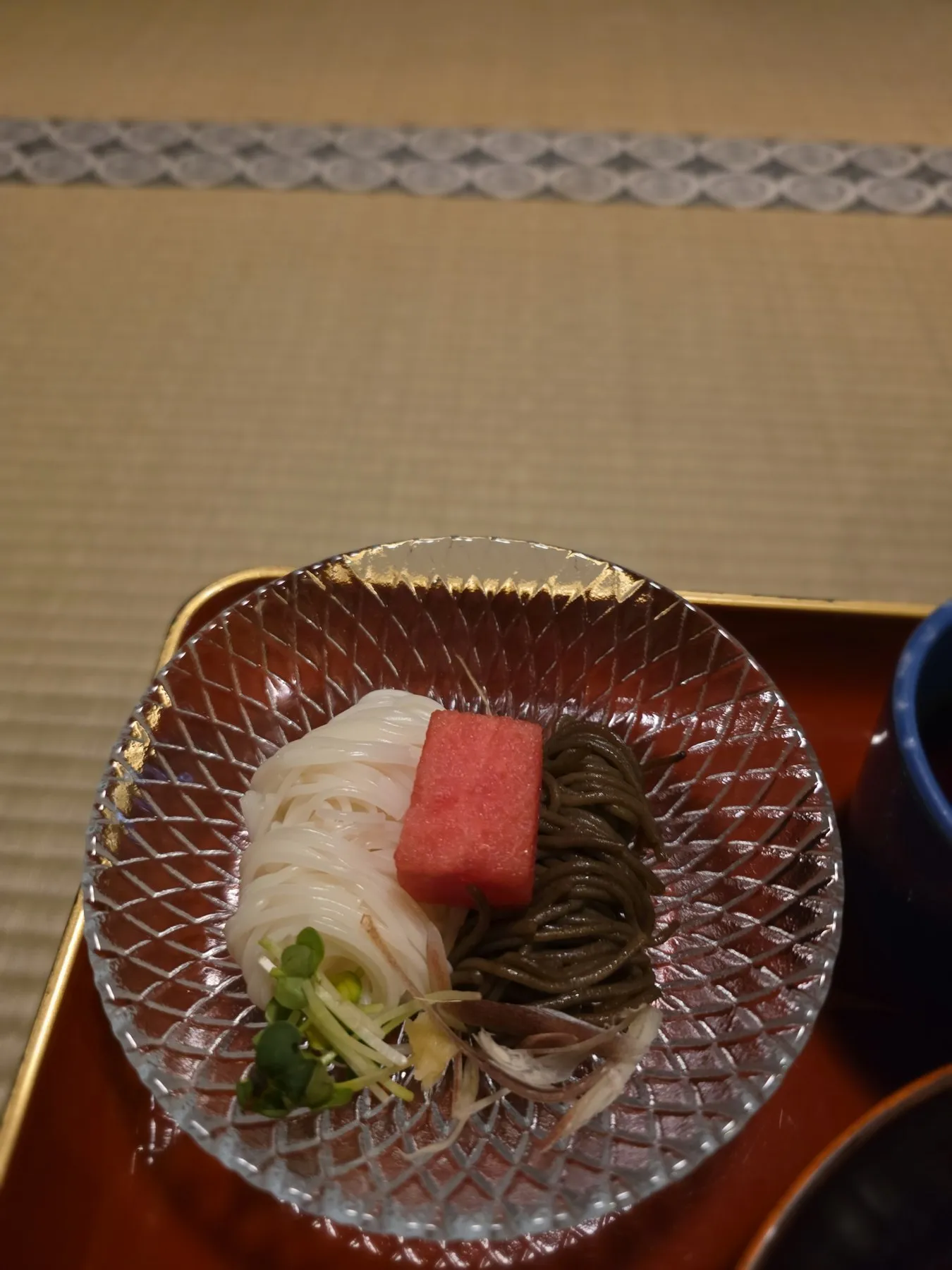 Glass bowl with a red cube, tea soba, and pickled greens