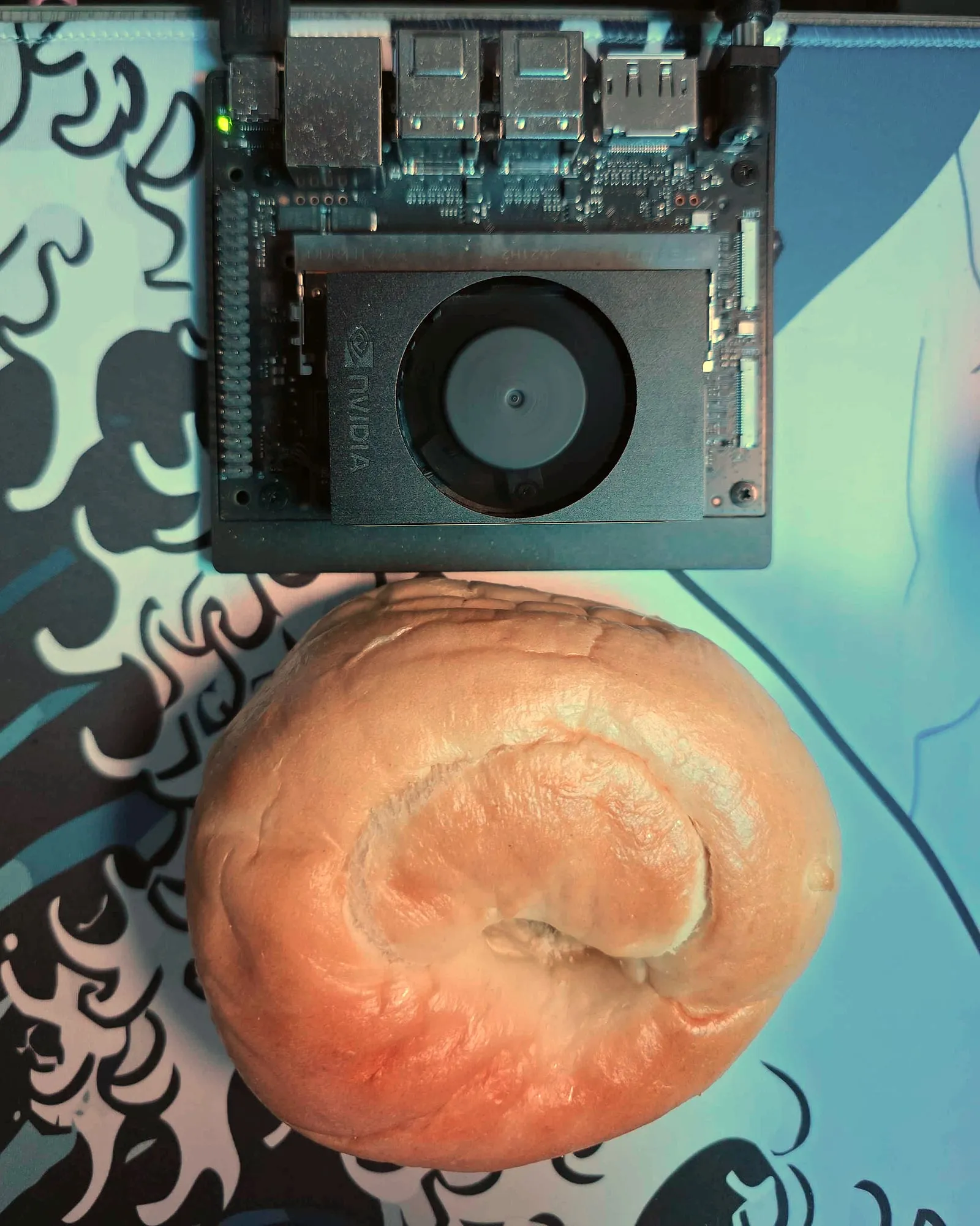 An NVIDIA Jetson Orin Nano developer kit on a desk next to a bagel of roughly the same size